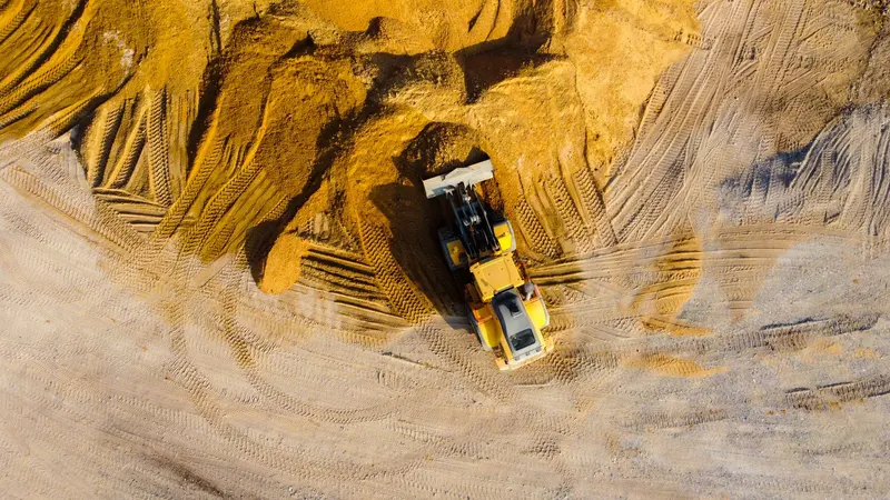 Wheel loader working a large sand and fill stockpile, seen from above