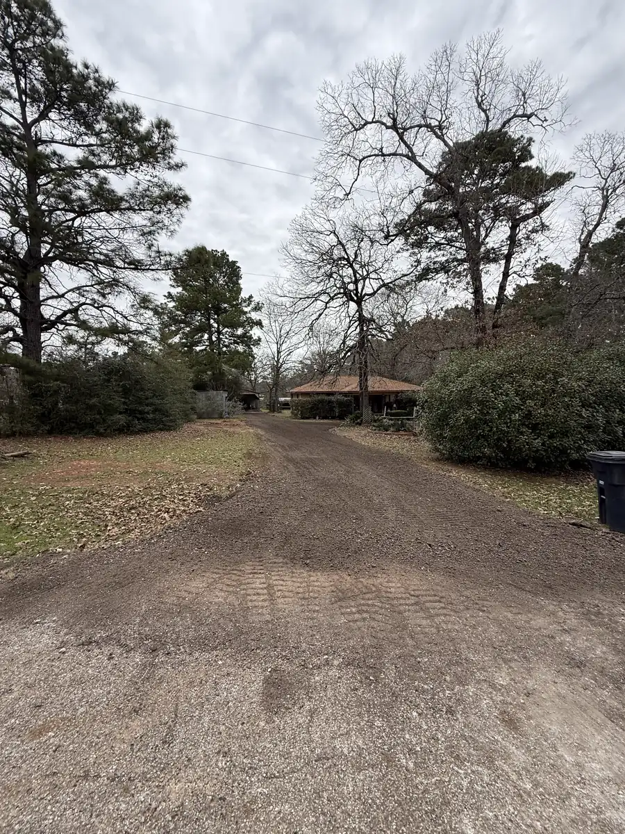 Driveway of loose milled asphalt newly spread toward a ranch house, surface still rough and open