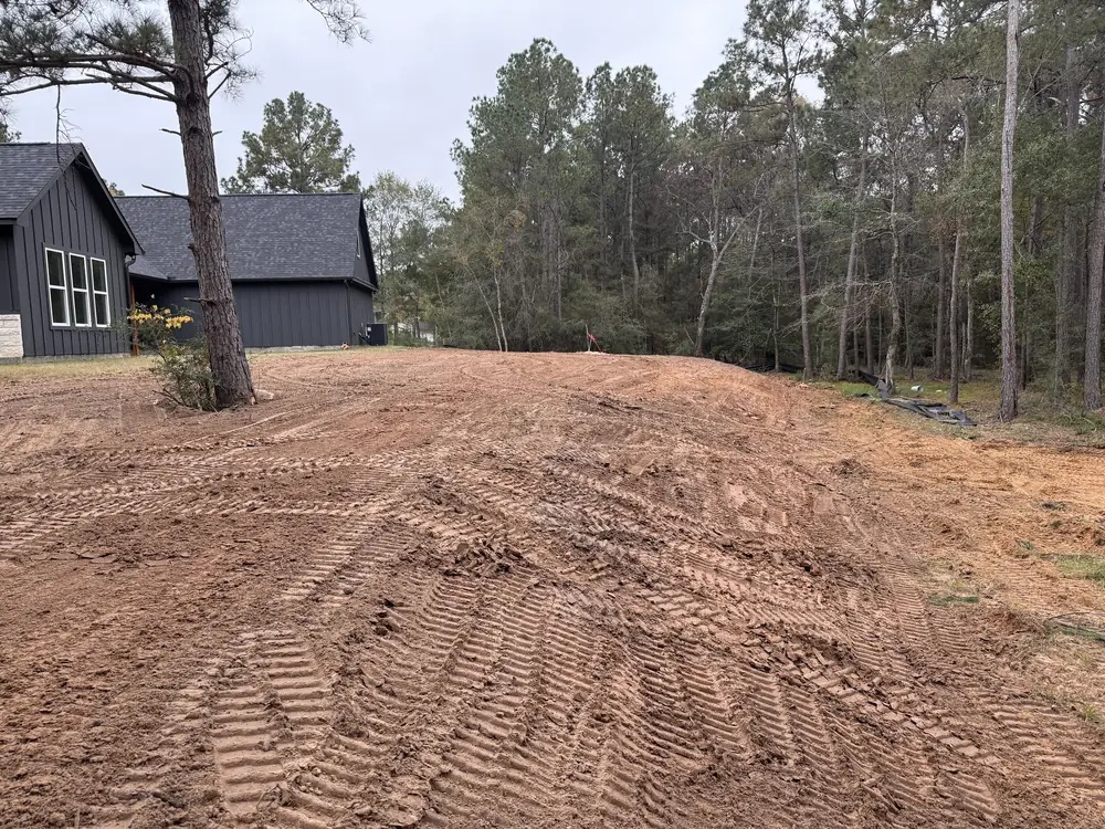 The same ground behind the same house graded flat with imported fill, track marks running across fresh orange dirt
