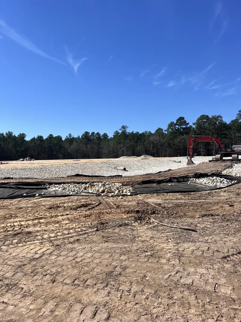 Excavator working a long windrow of white bull rock spread over black geotextile fabric across a cleared site