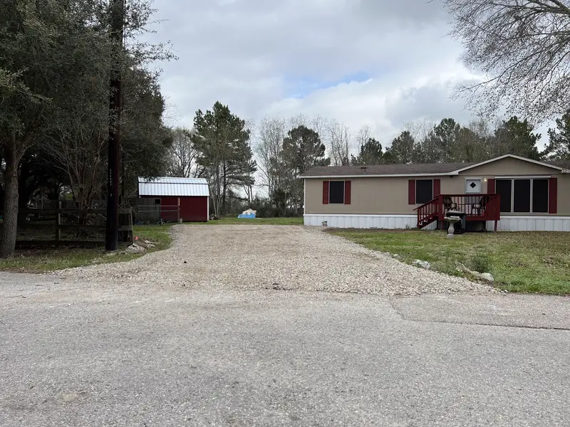 New crushed concrete driveway running from the county road past a red and white metal barn to a tan manufactured home