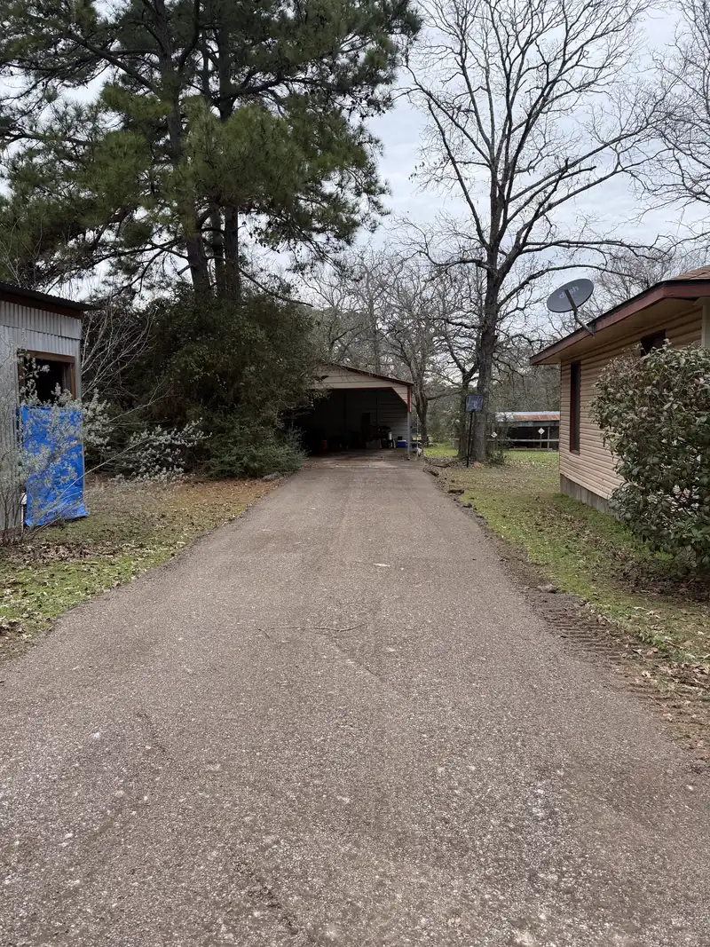 Milled asphalt driveway packed down smooth and dark, running between a shop and a house