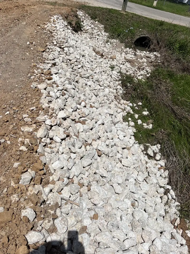 White limestone rip rap laid down the bank of a roadside ditch to armor it against washout, culvert pipe visible at the end